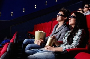 Two teens wearing 3D glasses watching a movie in a theater.